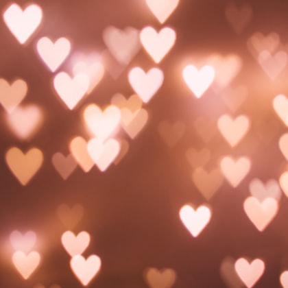 Softly blurred glowing heart shapes floating against a warm rose-pink background