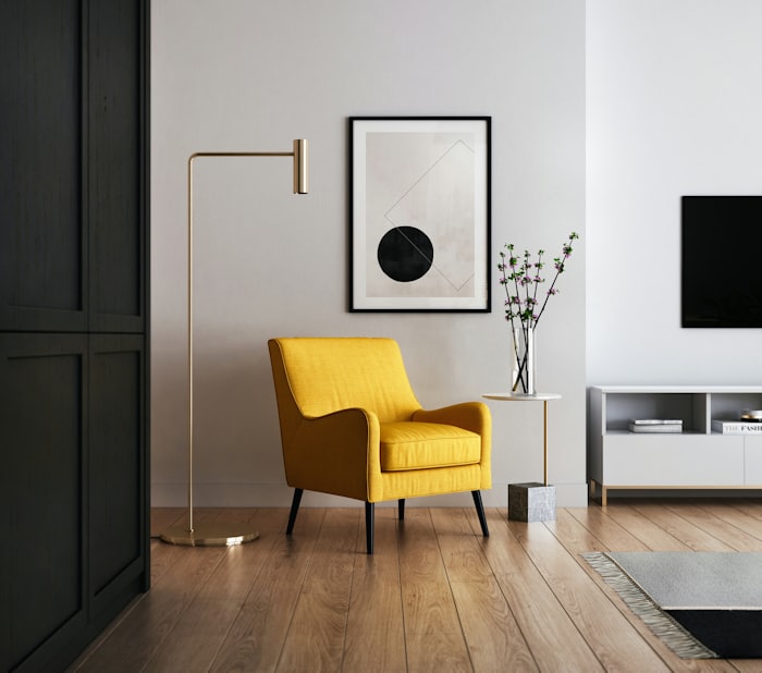 A minimalist living room with a bright yellow armchair, slim floor lamp, framed art, and a small vase of blossoms