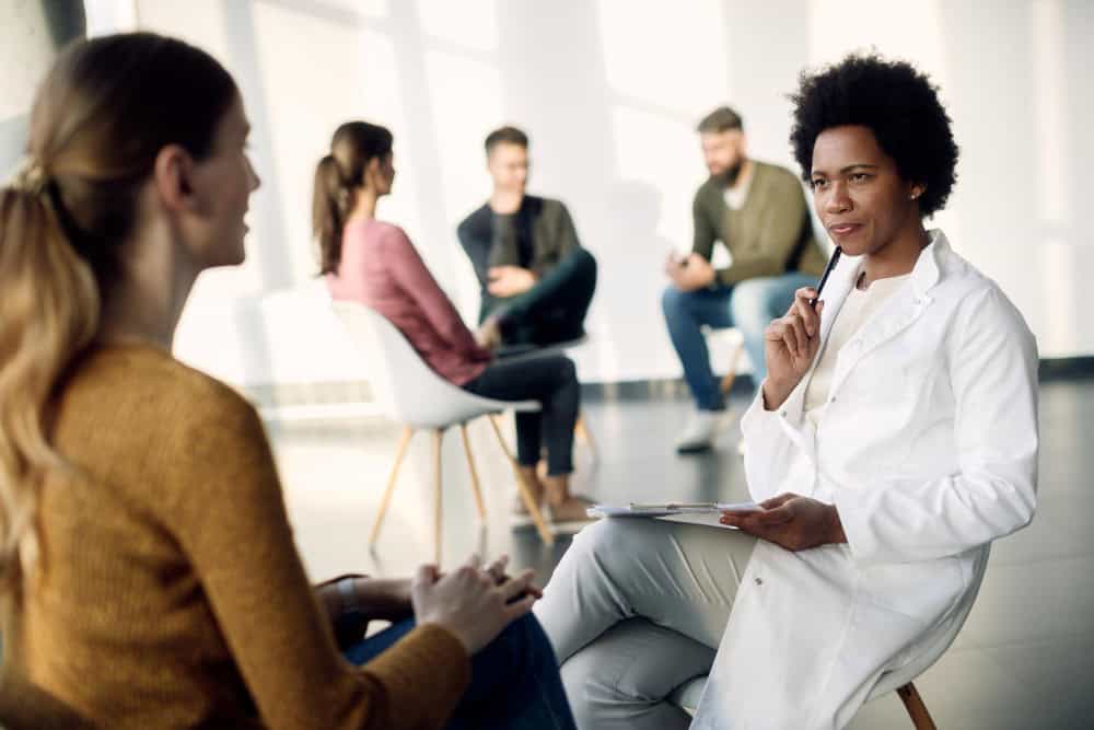 Black female doctor speaking with a woman during a group psychotherapy session in Elk Grove Village, IL.