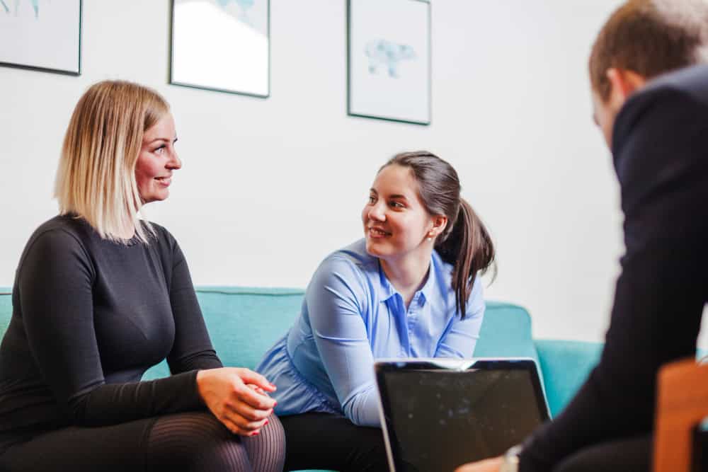 Women sitting together on a couch and smiling during addiction treatment in Arlington Heights, IL.
